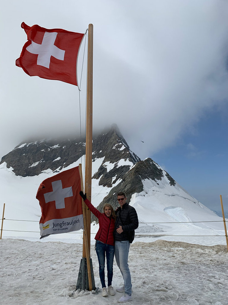 Man and woman stand in front of Swiss Flag in Switzerland at Jungfraujoch