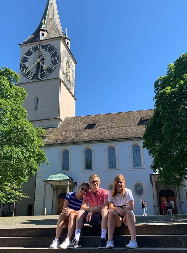 Three kids sitting in front of St. Peter's church in Zurich, Switzerland
